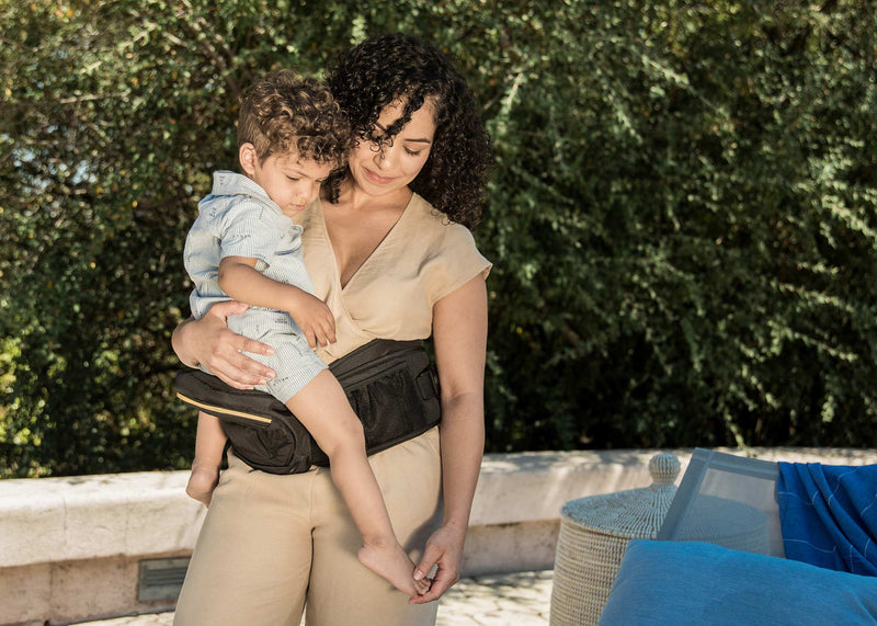 Parent holding and kissing a sleeping baby in a black baby wrap carrier, showing closeness and comfort.