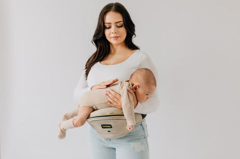 Parent supporting baby on their stomach across a Tushbaby Hip Carrier seat for burping after feeding.