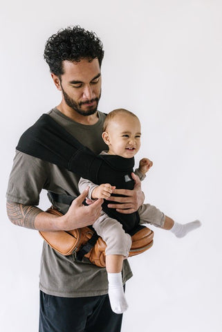 Parent carrying baby in an outward-facing position using the Tushbaby Hip Carrier with The Hip Seat Hands-Free Attachment, showing hands-free comfort and support.